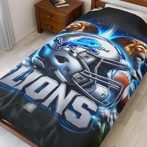May include: A blue and silver football helmet with the word "LIONS" in large, silver letters dominates a black blanket. Two lion heads and a football are also featured. The blanket is on a bed.