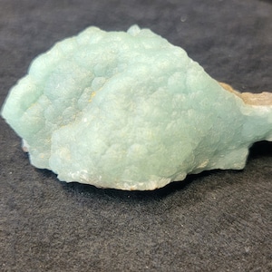 May include: A large, light green, mineral specimen with a rough, textured surface. The mineral has a cluster of small crystals.