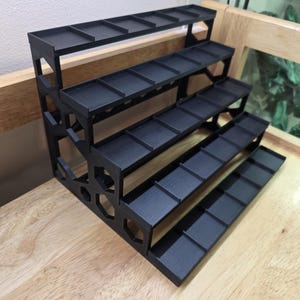 May include: A black tiered display stand featuring four levels with individual compartments separated by dividers. The side panels have a geometric hexagonal cutout pattern. The text Terrapin Minerals is printed in the bottom right corner.