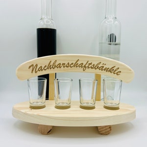 Könnte beinhalten: Holz-Schnapsglas-Halter mit dem Text "Nachbarschaftsbänkle" auf der Oberseite. Der Halter hat vier Schnapsgläser und zwei Flaschen an der Seite.