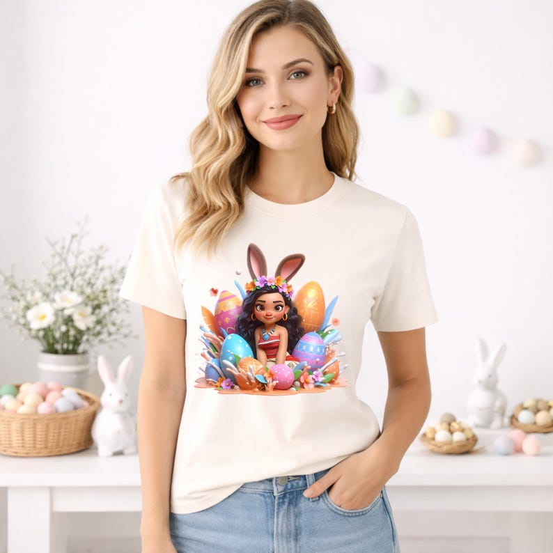 May include: Cream-colored t-shirt featuring a cartoon illustration of a girl with bunny ears, surrounded by Easter eggs and flowers. The design includes vibrant colors like blue, orange, and pink, creating a festive and cheerful aesthetic.