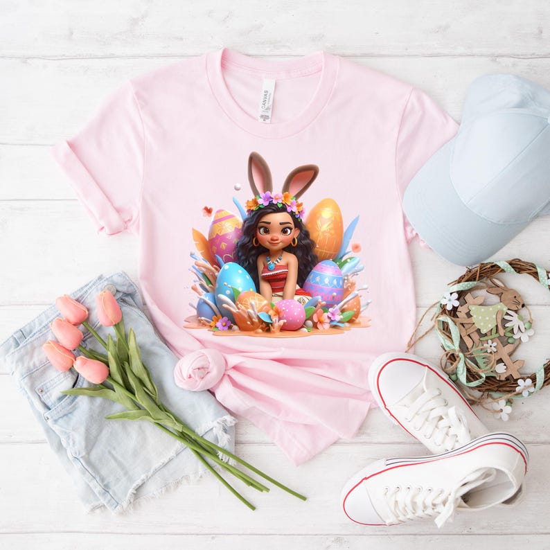 May include: A light pink t-shirt featuring a cartoon illustration of a woman with bunny ears surrounded by Easter eggs. The image includes a pair of blue denim shorts, a white baseball cap, a wreath, a pair of white sneakers, and a bouquet of pink tulips.