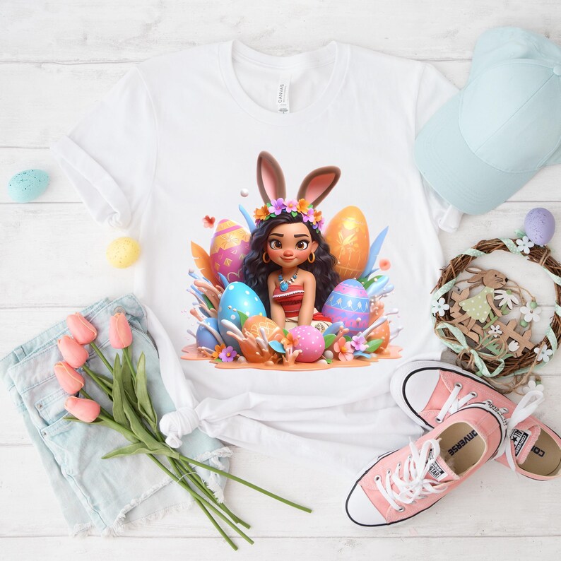 May include: White t-shirt featuring a cartoon character with bunny ears and Easter eggs. The design includes a floral crown and colorful eggs. Pink sneakers, a light blue cap, and a decorative wreath are also visible.
