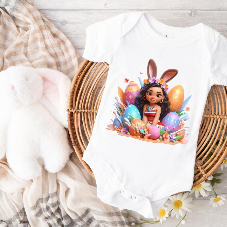 May include: White baby onesie with a colorful graphic of a cartoon character wearing bunny ears and surrounded by Easter eggs. The onesie is on a woven basket with a white stuffed bunny and a beige and white patterned cloth.
