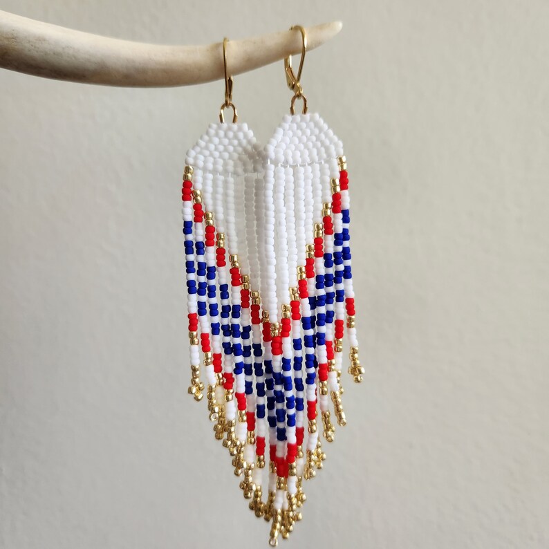 May include: White, red, and blue beaded earrings with gold accents. The earrings are long and dangle, with a chevron pattern.