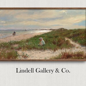 May include: A framed landscape painting depicts a beach scene with a person on horseback and another person near the dunes. The artwork features a sandy beach, green dune grass, and a cloudy sky. The frame is a dark brown color. The text "Lindell Gallery & Co." is at the bottom.