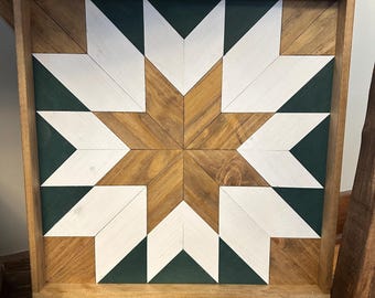 Puede incluir: Una pieza de arte de pared enmarcada en madera con un diseño geométrico que presenta una forma de estrella en el centro. La estrella está hecha de madera marrón y está rodeada de triángulos blancos y verde oscuro.