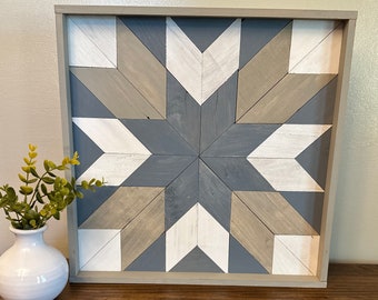 Puede incluir: Una pieza de arte de pared de madera enmarcada con un diseño de estrella geométrica en tonos de gris, blanco y marrón.