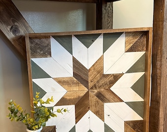Puede incluir: Una pieza de arte de pared enmarcada en madera con un diseño de estrella geométrica en tonos marrones, blancos y verdes. La estrella está hecha de varias piezas de madera y se coloca sobre un fondo blanco.
