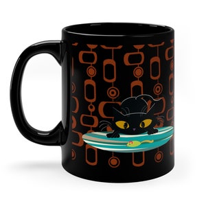 Puede incluir: Taza de café de cerámica negra con un gato negro en una tabla de surf con un pez verde. El fondo es un patrón geométrico negro y naranja.