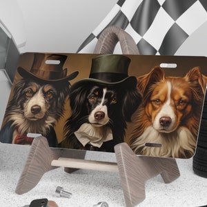 May include: Three dogs wearing top hats and bow ties. The dogs are a black and white border collie, a black and white Australian Shepherd, and a brown and white Australian Shepherd. The dogs are on a brown background with a gold frame.