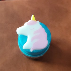 Puede incluir: Un tapón de botella de unicornio azul y rosa con un cuerno amarillo.