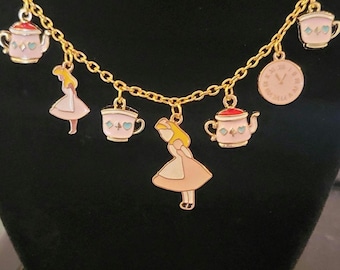 Può includere: Una collana a catena dorata con più ciondoli, tra cui una tazza da tè, una teiera, un personaggio di Alice nel Paese delle Meraviglie e un orologio. I ciondoli sono rosa, blu e gialli con accenti dorati.