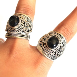 May include: Two silver rings with black gemstones set in ornate silver settings. The rings are worn on a person's fingers.