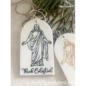 May include: White keychain with a black line drawing of Jesus Christ on a white background. The keychain has a silver key ring and the text "Think Celestial" is printed below the image.
