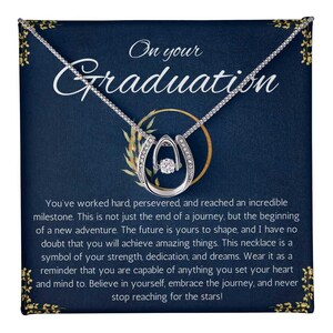 May include: A silver necklace with a horseshoe pendant and a small clear crystal in the center. The necklace is displayed on a blue card with the text "On your Graduation" and a message about working hard and achieving dreams.