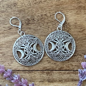 May include: Silver earrings with a circular design featuring a tree of life, three crescent moons, and a pentagram. The earrings have a hook closure.
