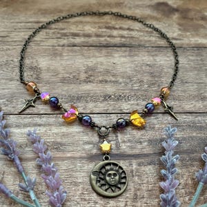 Op de afbeelding: Een hemels thema ketting van brons. Het heeft een hanger met zon en maan, sterbedels en iriserende kralen. De ketting is versierd met vlindervormige kristallen.