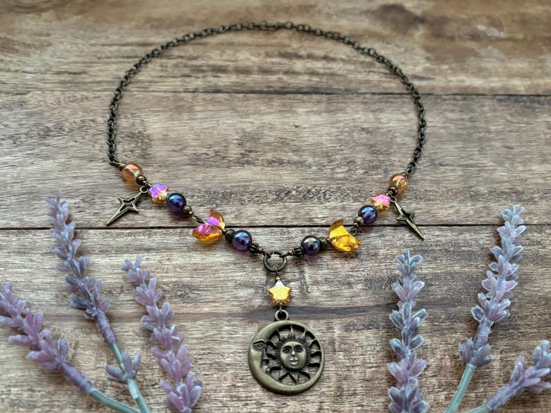 Op de afbeelding: Een hemels thema ketting van brons. Het heeft een hanger met zon en maan, sterbedels en iriserende kralen. De ketting is versierd met vlindervormige kristallen.