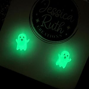 May include: Glow-in-the-dark ghost earrings. Each earring features a small, friendly ghost design that glows bright green. The earrings are displayed on a light-coloured card with the text "Jessica Ruth Creations" in a circular logo.