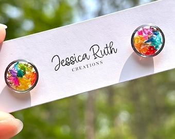 May include: Stud earrings with a circular design, featuring a colourful floral arrangement. The earrings have a clear resin dome over a mix of pink, orange, yellow, green, and blue petals. The earrings are on a white card with the text "Jessica Ruth Creations."