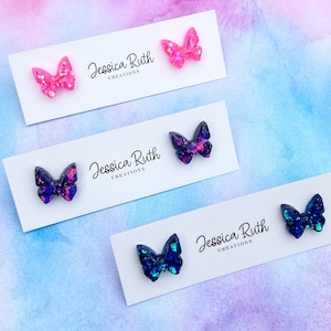 May include: Three pairs of butterfly earrings on white cards with the text "Jessica Ruth Creations". The earrings are made of resin and have a glittery finish. The butterflies are pink, blue, and black.