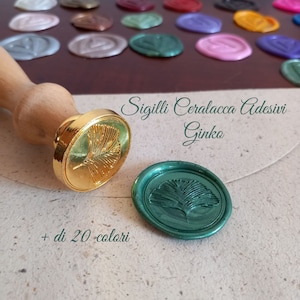 Könnte beinhalten: Goldene und grüne Wachssiegel mit einem Ginkgoblatt-Design. Der Text "Sigilli Ceralacca Adesivi Ginko + di 20 colori" ist unter den Siegeln gedruckt.