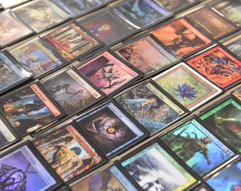 May include: A collection of Magic: The Gathering trading cards, displayed in protective sleeves. The cards feature various fantasy art illustrations, with a range of colors and designs. The cards are arranged in a grid-like pattern.