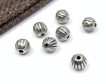 May include: Seven silver beads with a ridged surface and a hole in the center. The beads are arranged in a semi-circle on a white surface.