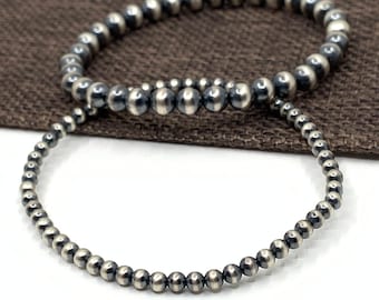 May include: Two silver bracelets with a beaded design. The bracelets are made of small, round beads that are silver in color. The beads are arranged in a circular pattern to form the bracelets.