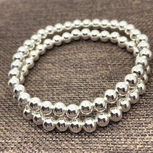 May include: Two silver bead bracelets stacked on top of each other. The beads are round and shiny.