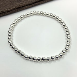 May include: A silver beaded bracelet with a simple design. The bracelet is made of small, round beads that are strung together on a thin cord.