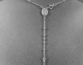 Puede incluir: Un collar de rosario plateado con un colgante de crucifijo. El collar presenta una serie de pequeñas cuentas redondas y un crucifijo detallado con una figura de Jesús. El diseño incluye una pieza central decorativa con una figura religiosa.