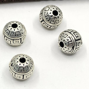 Peut inclure: Quatre perles rondes en argent avec un motif géométrique. Les perles ont un trou au centre pour être enfilées.