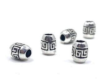 May include: Five silver-colored barrel beads with a geometric design. Each bead has a dark hole at each end and a repeating square pattern around the center. The beads are scattered on a white background.