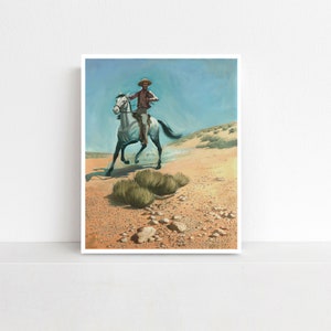 May include: An art print depicting a cowboy riding a gray horse through a desert landscape. The cowboy wears a brown shirt and hat. The background features a blue sky and tan desert terrain with sparse vegetation.