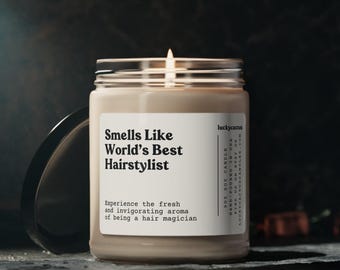 May include: A lit soy candle in a clear glass jar with a white label that reads Smells Like World's Best Hairstylist. The label includes the text Experience the fresh and invigorating aroma of being a hair magician and 9oz soy candle.