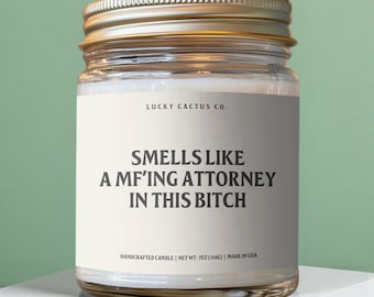 以下が含まれることがあります： 金色の蓋が付いた透明なガラス瓶のキャンドル。ラベルには「LUCKY CACTUS CO.」と「SMELLS LIKE A MF'ING ATTORNEY IN THIS BITCH」と書かれています。キャンドルは手作りで、重さは198gです。