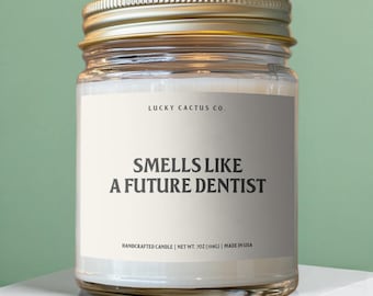 May include: A glass jar candle with a gold lid. The label reads "LUCKY CACTUS CO." and "SMELLS LIKE A FUTURE DENTIST." The candle is 7 oz (198g) and made in the USA. The background is a light green.