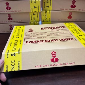 Può includere: Una scatola di cartone color marrone chiaro etichettata COLD CASE INVESTIGATION UNIT con un'icona rossa da detective. La scatola presenta nastro giallo stampato con la parola EVIDENCE e un timbro rosso EVIDENCE DO NOT TAMPER e un modulo di caso.