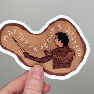 May include: A brown and white sticker with a drawing of a person in armor holding a knife. The text on the sticker reads "May thy knife chip & shatter".