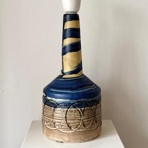 Może przedstawiać: Zestaw trzech ceramicznych kubków z nakrapianym, matowym wykończeniem. Kubki są w odcieniach kremu, jasnoszarym i ciemnoszarym. Każdy kubek ma prosty, minimalistyczny design.