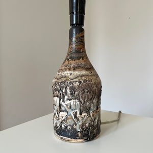Może przedstawiać: Ceramiczna lampa stołowa z brązową, białą i czarną glazurą. Lampa ma fakturowaną powierzchnię i czarny klosz.