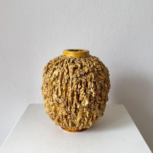 Może przedstawiać: Mały, okrągły, żółty wazon ceramiczny z fakturowaną powierzchnią. Wazon ma surowy, organiczny wygląd.
