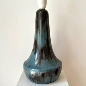 May include: A ceramic lamp base with a blue and black glaze. The base has a rounded bottom, a slender neck, and a white lamp socket. The lamp is approximately 12 inches tall.