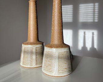 Puede incluir: Un par de lámparas de mesa de cerámica con un diseño de rayas marrones y blancas. Las lámparas tienen una base alta y delgada y una pantalla blanca.