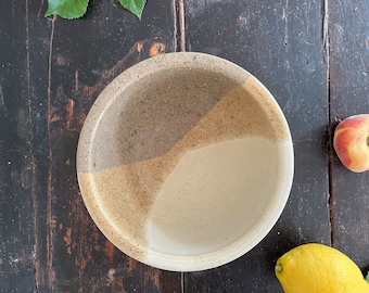May include: A ceramic bowl with a white, beige, and brown speckled glaze. The bowl has a rounded shape and a wide rim.