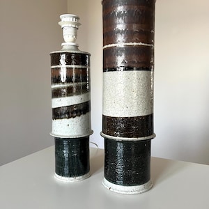 以下が含まれることがあります： 茶色、白、緑のストライプ模様のセラミック製テーブルランプが2つ。ランプは円筒形で、互いに積み重ねられています。