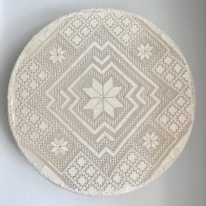 Peut inclure: Nappe ronde de couleur crème avec un motif de dentelle complexe. Le design présente une étoile centrale, entourée de formes géométriques et d'éléments floraux. La nappe est faite d'un tissu délicat à tissage ouvert.