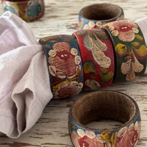 May include: A white ceramic mug with a black handle and the text "But First, Coffee" in a bold, black font. The mug is set against a blurred background, suggesting a cozy setting.